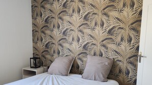 A bedroom with a bed, two pillows, a nightstand, and a wall with a leaf pattern.
