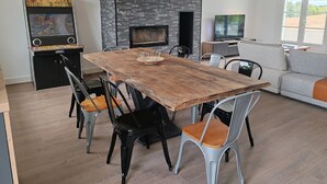 A modern living room with a wooden dining table, black and grey chairs, a grey sofa, a fireplace, and a television.