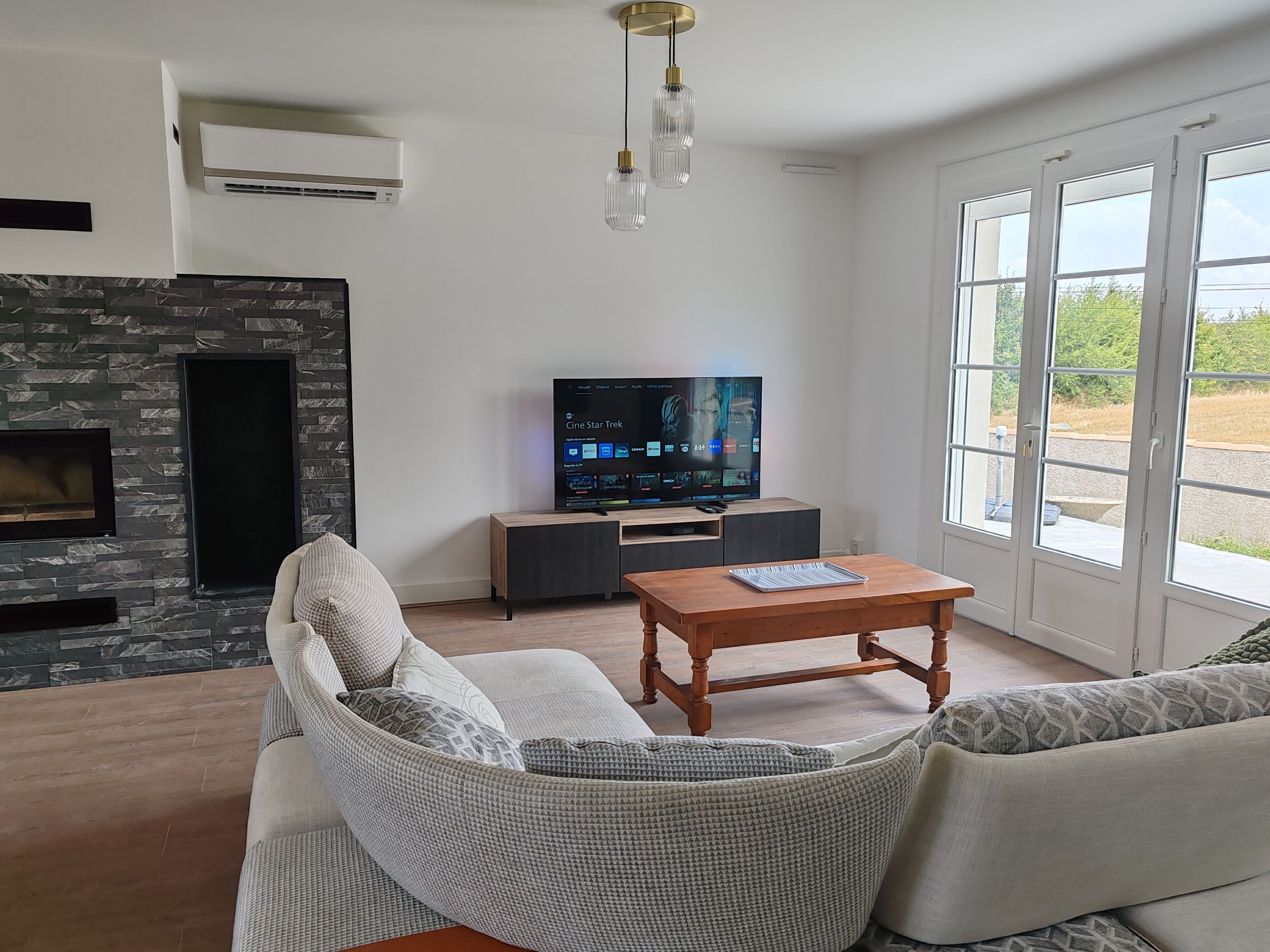 A modern living room with a stone fireplace, a large flat-screen TV, a comfortable sofa, and a wooden coffee table.