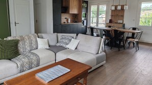 A modern living room with a sectional sofa, a wooden coffee table, and a dining area with a wooden table and chairs.