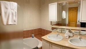 Un baño con dos lavamanos, una bañera y un espejo.
