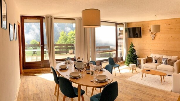 Una sala de estar moderna con comedor, ventanas amplias, un televisor de pantalla plana y un árbol de Navidad.