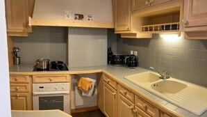 Una cocina compacta con alacenas de madera, estufa, pileta y cafetera.