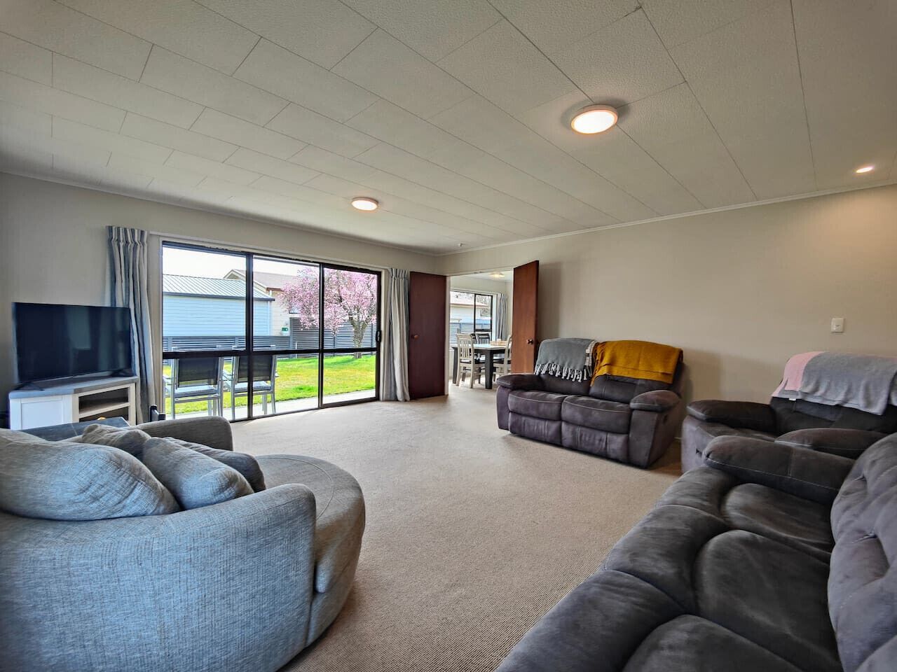 A spacious living room with a large TV, comfortable seating, and a view of the outdoors.
