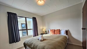 A bedroom with a large bed, a nightstand, a lamp, and a window with curtains. - Luxmore Lookout Te Anau (Te Anau)