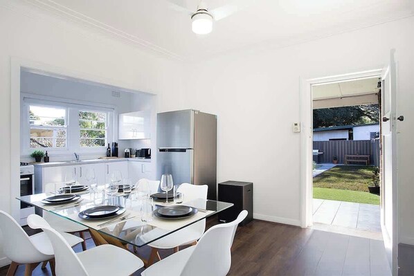 A modern kitchen with white cabinets, a built-in fridge, and a dining area with a glass table and white chairs.