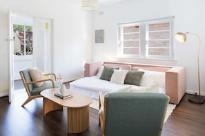 A cozy living room with a sofa, two chairs, a coffee table, a lamp, and a window with blinds.