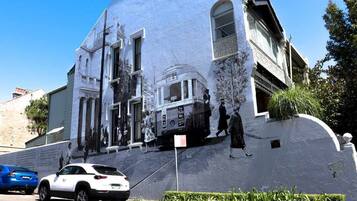 A building with a mural, a parked car, and a street sign.