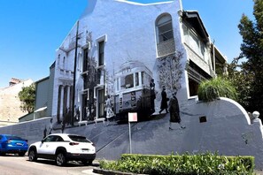 A building with a mural, a parked car, and a street sign.