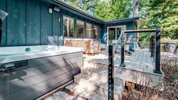 Une terrasse extérieure moderne dotée d’un jacuzzi, de sièges en bois et d’un escalier menant à un espace abrité.