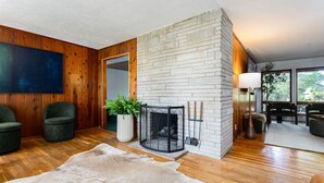 Un salon avec une cheminée, des murs en bois, une grande moquette et un téléviseur à écran plat.
