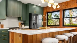 Une cuisine dotée d’un îlot central, de tabourets de bar, d’une grande fenêtre et de meubles de rangement en bois.
