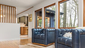 Un salon moderne avec des canapés en cuir, un plancher en bois et de grandes fenêtres donnant sur la verdure.