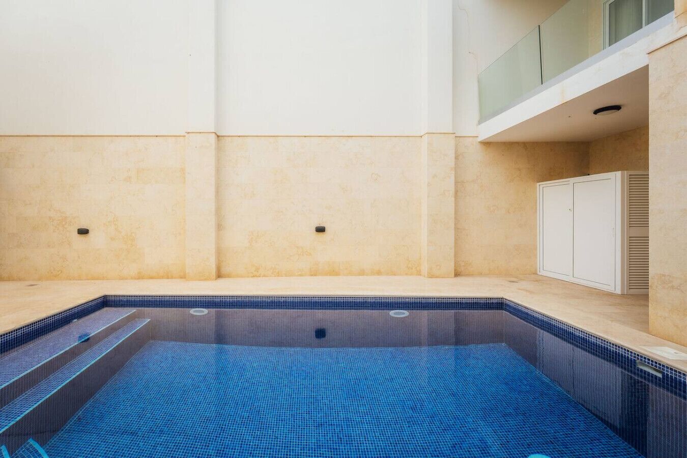 Ein Schwimmbecken mit gefliestem Boden und Wänden, einem kleinen Fenster und einer weißen Tür.