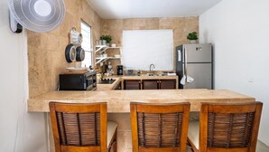 Een kleine keuken met een centraal eiland, een koelkast en een ventilator.