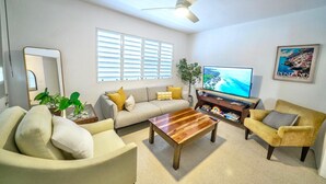 Een woonkamer met een bank, fauteuils, een salontafel, een televisie en een plafondventilator.