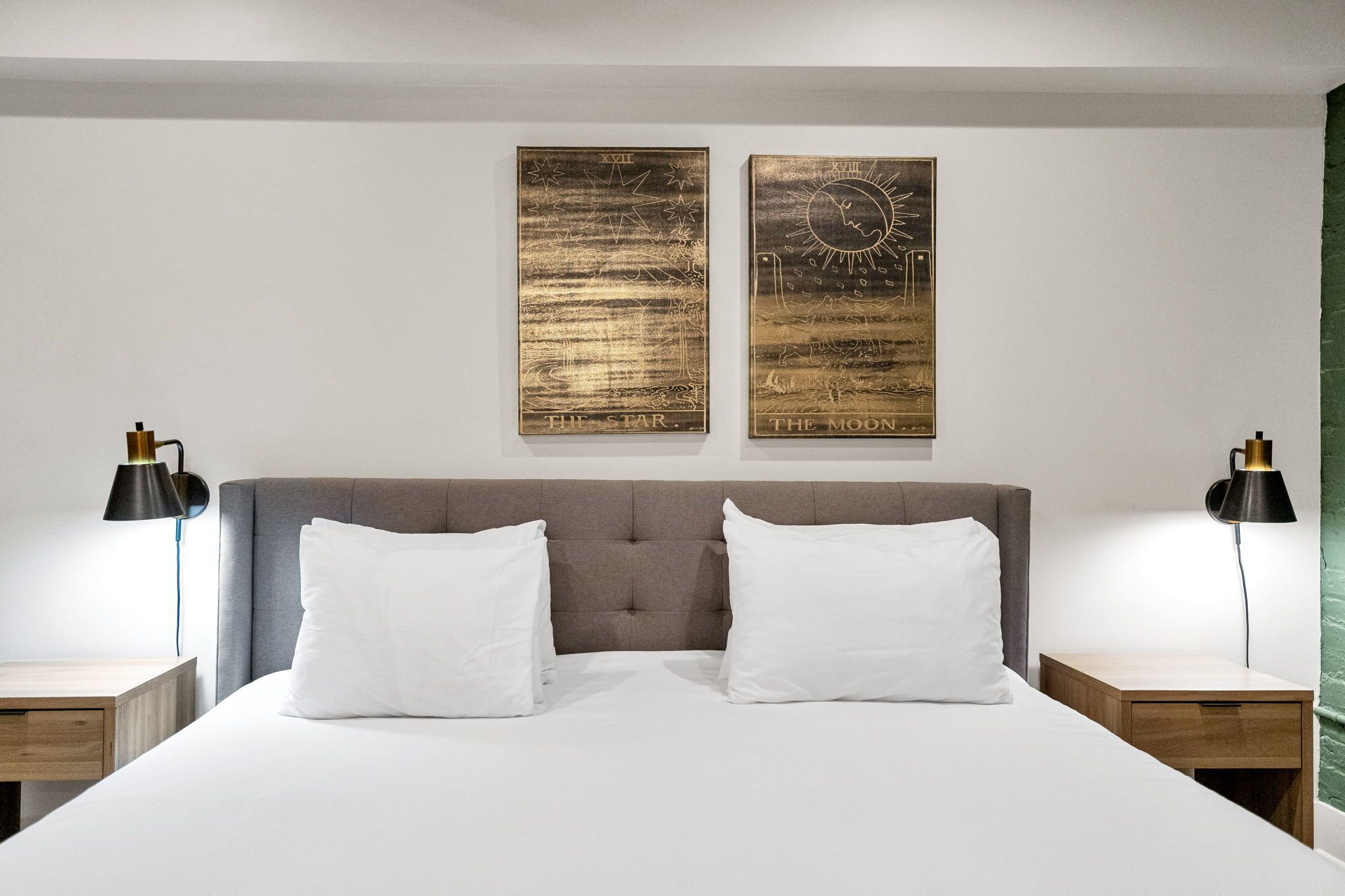 A neatly made bed with two white pillows, a grey upholstered headboard, and two bedside tables with black lamps.
