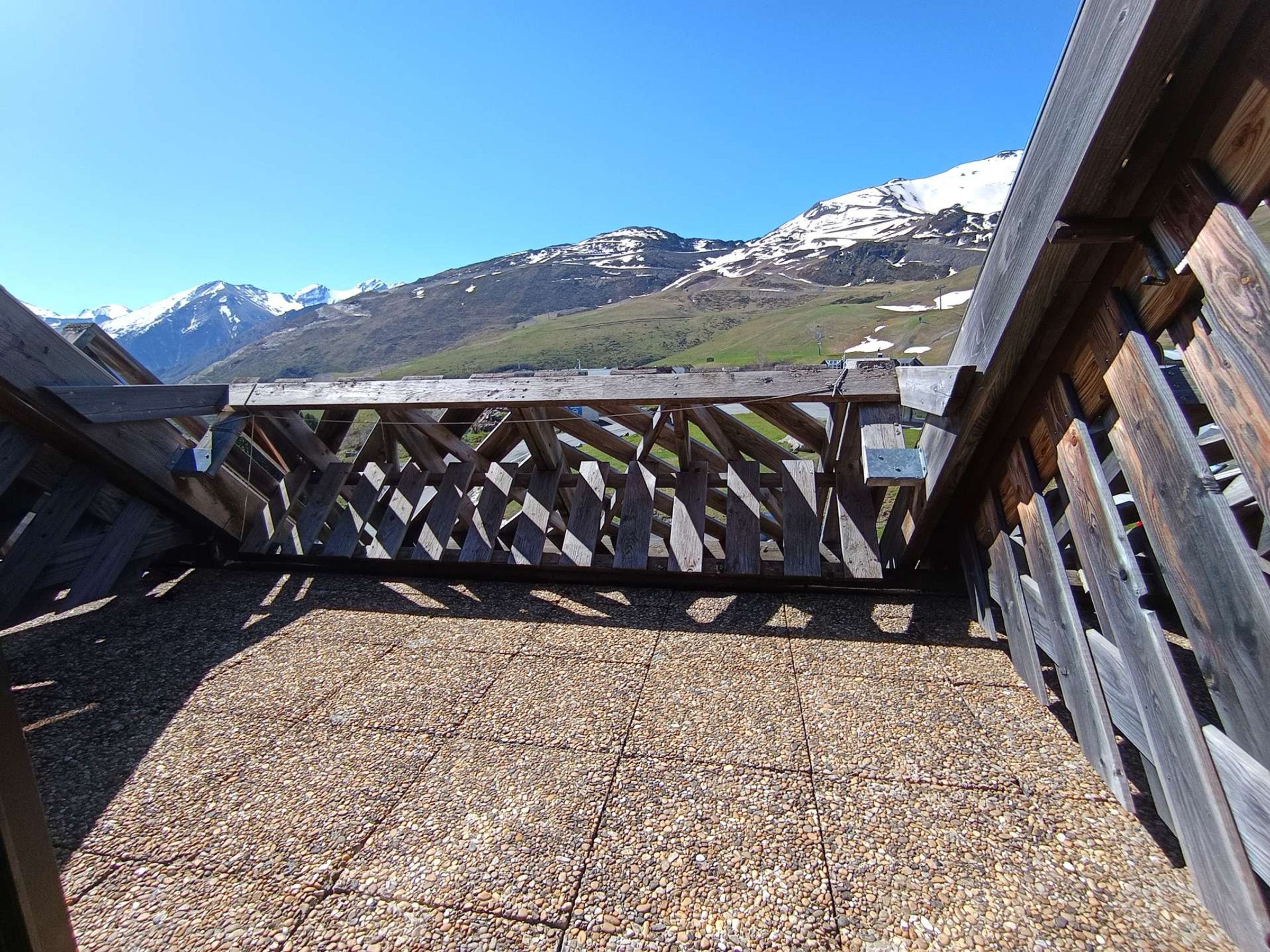 A wooden deck with a lattice railing, gravel flooring, and a view of snow-capped mountains in the background.