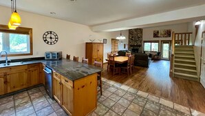 A spacious kitchen with wooden cabinets, a central island, and a dining area with chairs and a table. - Affordable Slope-Side: 3BR Condo w/ Private Hot Tub, Gas Fireplace, Great Location & Views. (Kimberley)