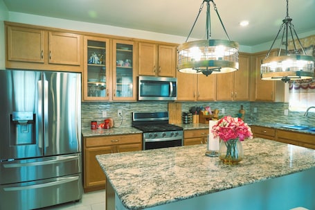 A modern kitchen with granite countertops, stainless steel appliances, wooden cabinets, and pendant lighting.