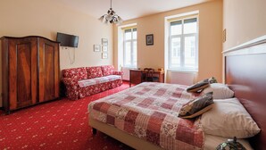 Ein Schlafzimmer mit einem großen Bett, einem Holzschrank, einem roten Blumensofa, einem Schreibtisch und einem Fernseher.