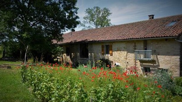A stone house with a tiled roof, a balcony, and a garden with red flowers. - Gite de l'arbre-lune (Rosay)