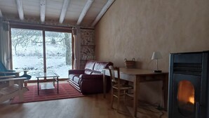 A cozy living room with a fireplace, wooden furniture, and a large window offering a view of a snowy landscape. - Gite de l'arbre-lune (Rosay)