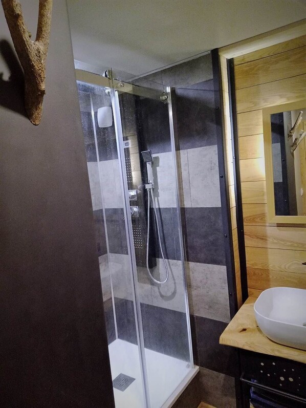 A shower with a glass door, a white sink, and a wooden vanity.
