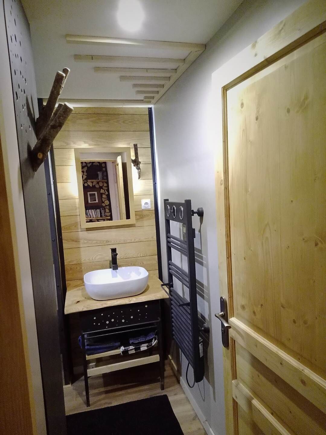 Een smalle badkamer met een houten wastafelmeubel, een witte wasbak en een handdoekhouder.