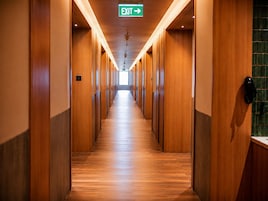 A hotel corridor with wooden walls and a wooden floor, leading to an exit sign.