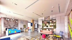 Un hall d’hôtel moderne comprenant un comptoir d’accueil, un espace salon et des plantes décoratives.