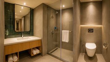 Un baño moderno con ducha de vidrio, lavamanos con espejo e inodoro.