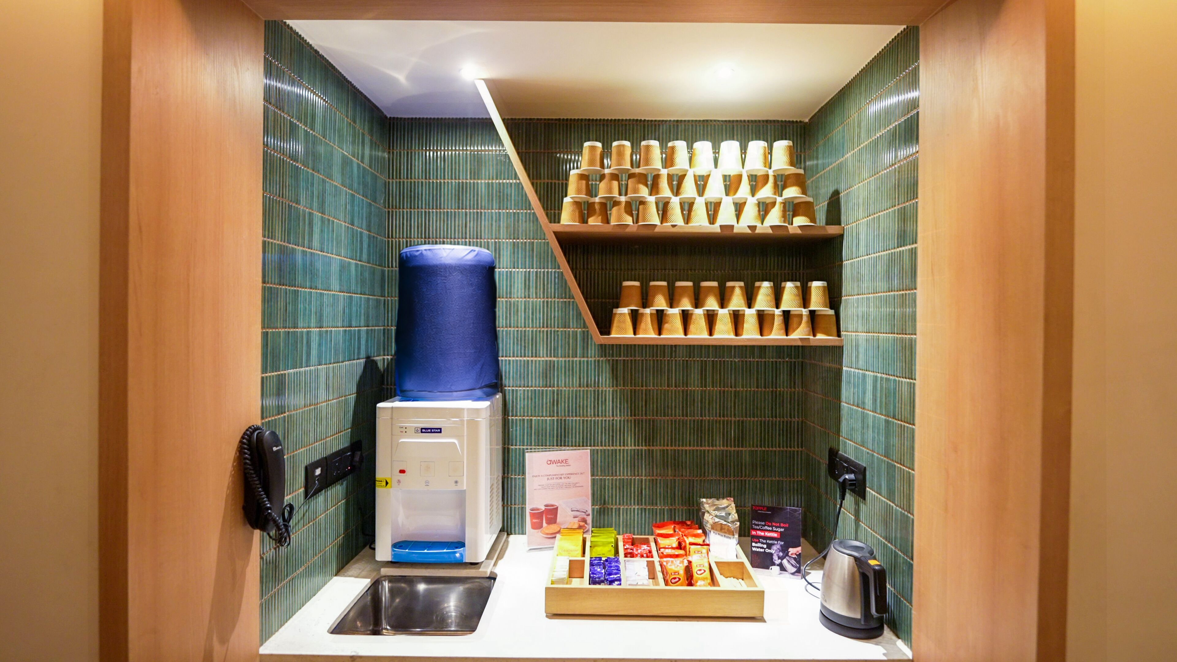 A compact kitchenette with a coffee machine, a water dispenser, a kettle, and a shelf with coffee cups.