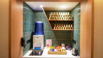A compact kitchenette with a coffee machine, a water dispenser, a kettle, and a shelf with coffee cups.