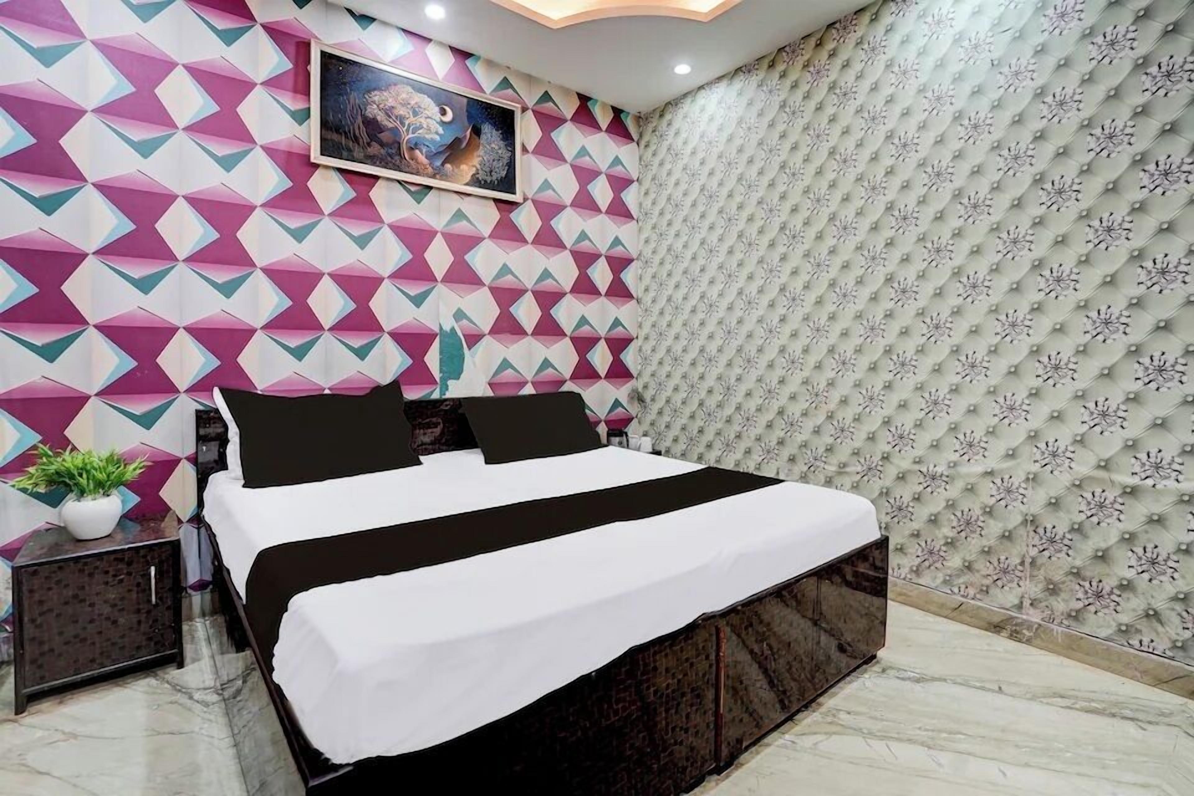 Een moderne slaapkamer met een wand met een geometrisch patroon, een groot bed met zwart-wit beddengoed, een klein nachtkastje met een plant en een decoratief schilderij boven het bed.
