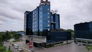 Un hôtel moderne, reconnaissable à son grand panneau « OLIVIA » placé en haut de la façade, qui se distingue par sa façade en verre et sa cour intérieure, agrémentée d’une zone pavée et de véhicules stationnés.