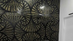 Un lit bien fait, avec du linge de lit blanc et des oreillers, une tête de lit capitonnée et un mur orné d’un motif géométrique.