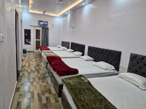 A hotel room with three beds, each with a different colored blanket, a television on the wall, and a checkered floor.