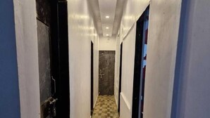 Un couloir étroit, doté d’un sol à carreaux, de murs blancs et d’une porte au fond, qui donne sur une pièce dont l’un des murs est en marbre.