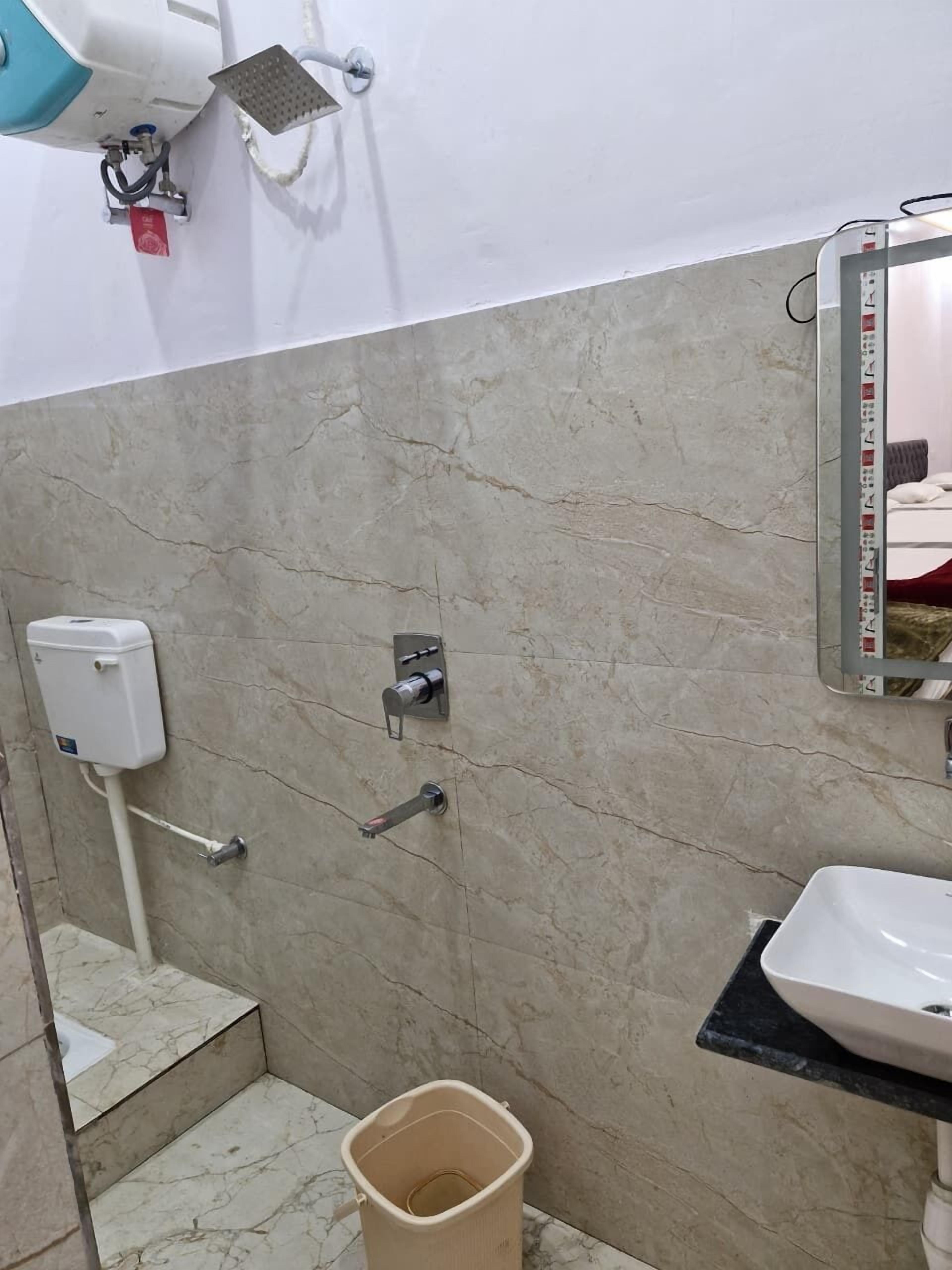 A bathroom with a marble-tiled wall, a white sink, a handheld showerhead, a soap dispenser, and a trash bin.