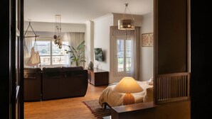 A modern hotel room with a sofa, a bed with a lamp, a TV, and a view of the city. - The Nile Magical Stay! (Cairo)