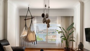 A living room with a hanging chair, a potted plant, a sofa, and a view of a cityscape through a large window. - The Nile Magical Stay! (Cairo)
