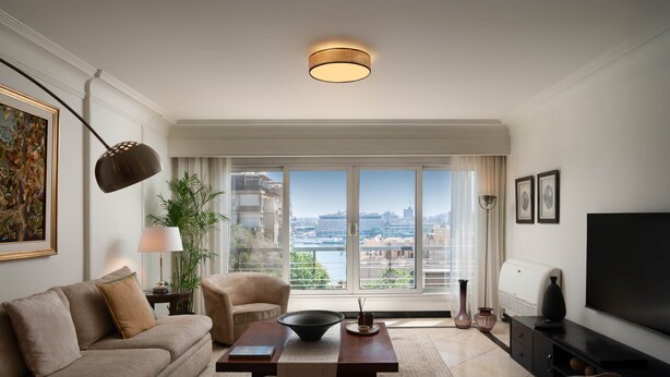 A modern living room with a sofa, coffee table, and a television. A large window offers a city view. - The Nile Magical Stay! (Cairo)