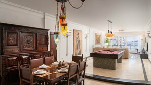 A dining area with a wooden table set for four, a pool table, and a view of the city through large windows. - The Nile Magical Stay! (Cairo)