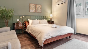 A neatly arranged bedroom with a wooden bed, a green headboard, a bedside table with a lamp, and a potted plant. - The Vintage Sunshine (Cairo)