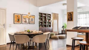 A dining area with a round table, four chairs, and a chandelier. There is a bookshelf with various items and a framed picture on the wall. - The Vintage Sunshine (Cairo)