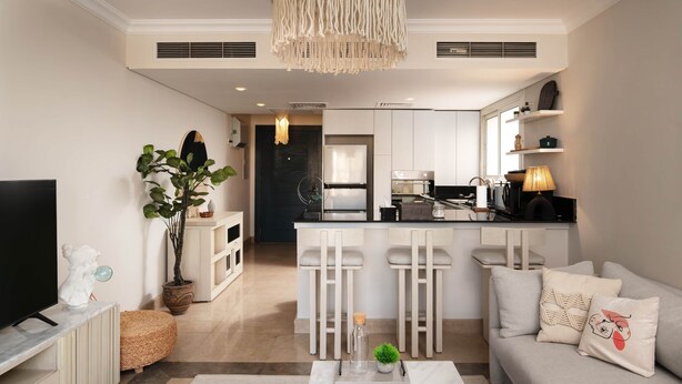 A modern living room with a sofa, a TV, and a dining area with bar stools. - New Giza’s Boho Bliss (6th of October City)