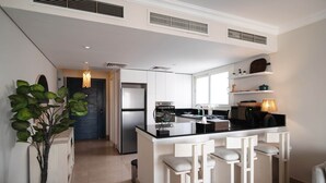 A modern kitchen with white cabinetry, a black countertop, and a bar area with white stools. - New Giza’s Boho Bliss (6th of October City)