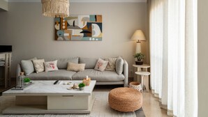 A modern living room with a neutral color palette, featuring a sofa, a coffee table, a hanging light fixture, and a painting on the wall. - New Giza’s Boho Bliss (6th of October City)