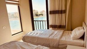 A hotel room with two beds, a balcony with a view, and a window. - Sunset Haven in Tawila TownHouse (Hurghada)